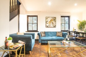 Un salon avec un canapé bleu, une table basse en verre et un coin repas comprenant une table et des chaises.