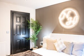 A bedroom with a black door, a neon sign, a potted plant, and a bed with multiple pillows. - Northern Hideaways, Apple Store, Ellingham (Chathill)