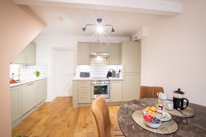A modern kitchen with light-colored cabinets, a built-in oven, and a dining area with a marble table set for breakfast.