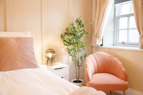 Une chambre à coucher avec un lit, une table de chevet avec une lampe, une plante en pot et une chaise rose.