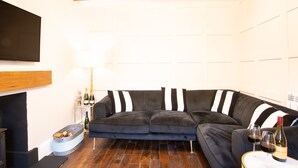 Una sala de estar moderna con un sofá modular gris oscuro, una chimenea, un cubo metálico con botellas, y una mesa con vasos y una botella.