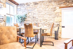Un comedor con paredes de piedra, una mesa y sillas, una planta en maceta y una puerta con una cesta de metal.