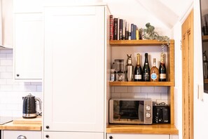 Una cocina con armarios blancos, un microondas, un tostador y una estantería con libros y botellas de vino.