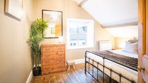 Un dormitorio con un aparador de madera, una planta en maceta, una cama con estructura metálica, una ventana y una lámpara en el techo.