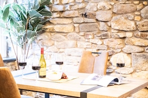 A table with a bottle of wine, glasses, a bowl of grapes, and a magazine.
