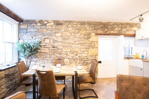 A dining area with a stone wall, wooden table, and brown chairs. - Northern Hideaways, St Cuthberts (Seahouses)