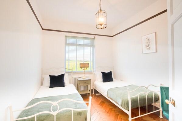 A bedroom with two beds, a window, a radiator, and a hanging light fixture.