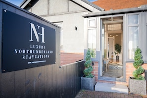 A luxury Northumberland staycation property with a prominent sign, a wooden fence, and a well-maintained entrance.