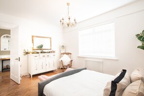 Une chambre à coucher avec un lit, une commode, une chaise, un miroir et une fenêtre.