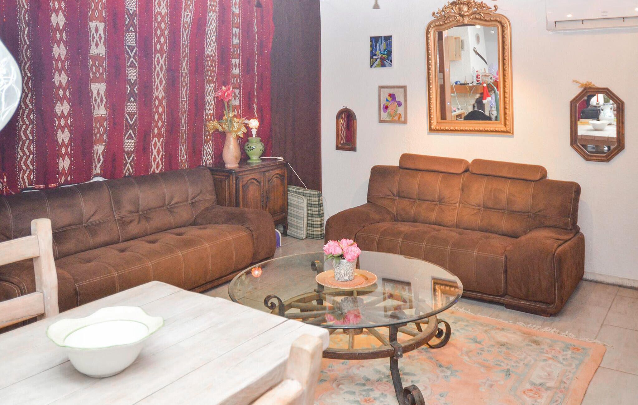 Ein Wohnzimmer mit zwei braunen Sofas, einem Glastisch und einem Teppich mit Blumenmuster.