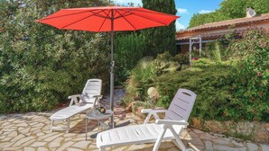 A patio with two white lounge chairs and a red umbrella, surrounded by greenery and a stone floor. - Pet friendly home in St Julien de Peyrolas (St Julien de Peyrolas)