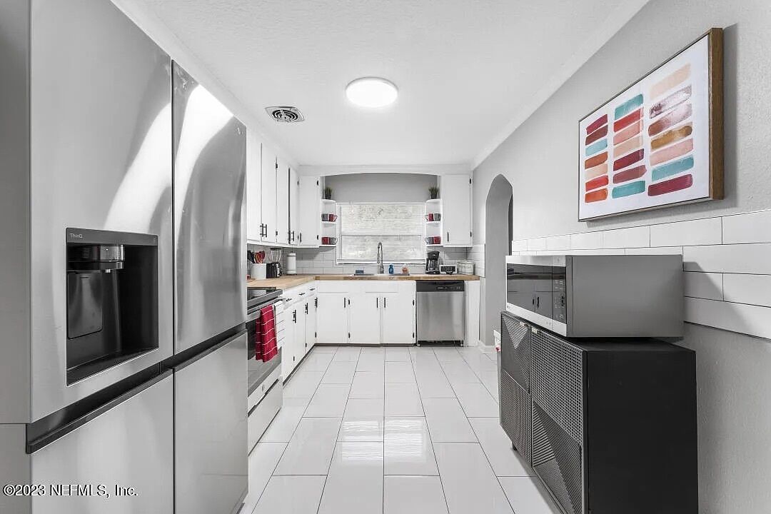 A modern kitchen with white cabinetry, stainless steel appliances, and a tiled floor.