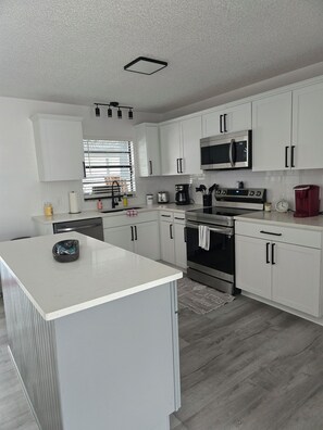 Enjoy cooking in this well-lit kitchen with an oven, stainless steel microwave, and a spacious island with a black bowl.