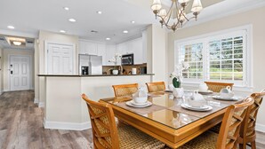 Una cocina moderna con armarios blancos, una isla central y un comedor con una mesa de vidrio y sillas de madera.