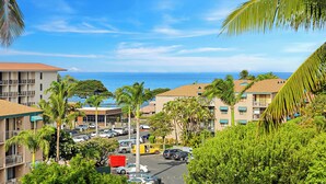 A coastal hotel with multiple floors, a parking lot, and a view of the ocean.