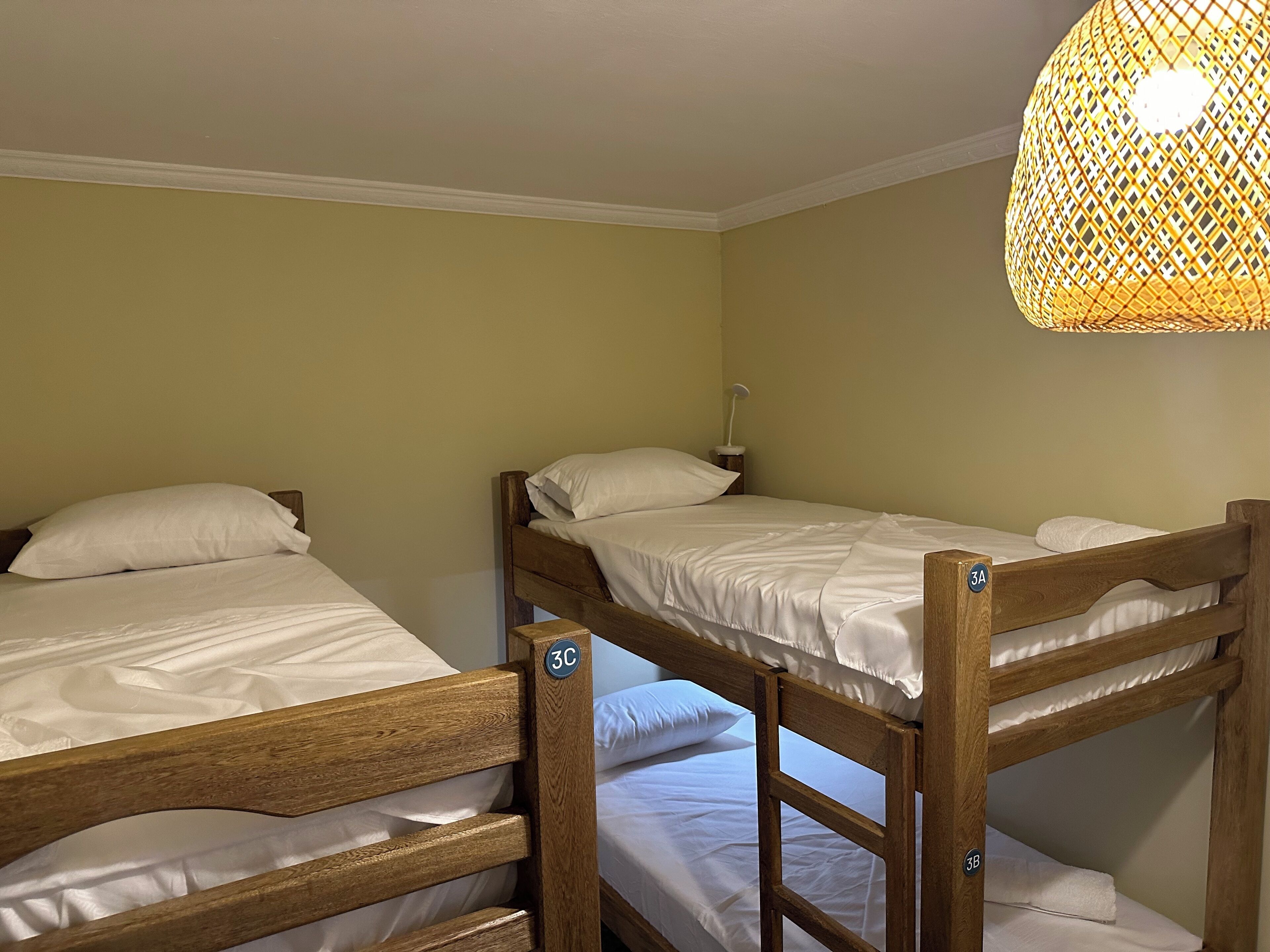 A dormitory room with bunk beds, a small bedside table, and a hanging light fixture.