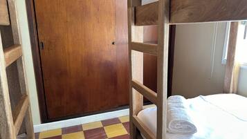 A bunk bed room with a checkered floor, wooden door, and a window with curtains.