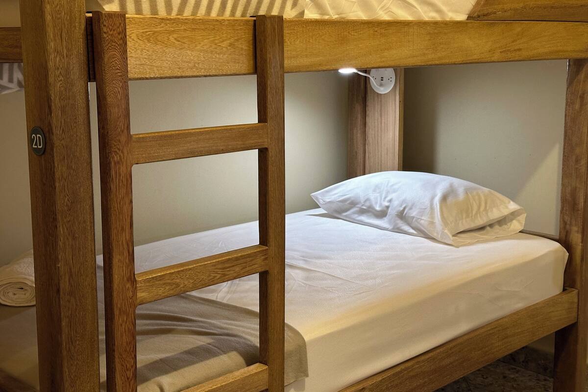 A bunk bed with a wooden frame, a white mattress, and a single white pillow.
