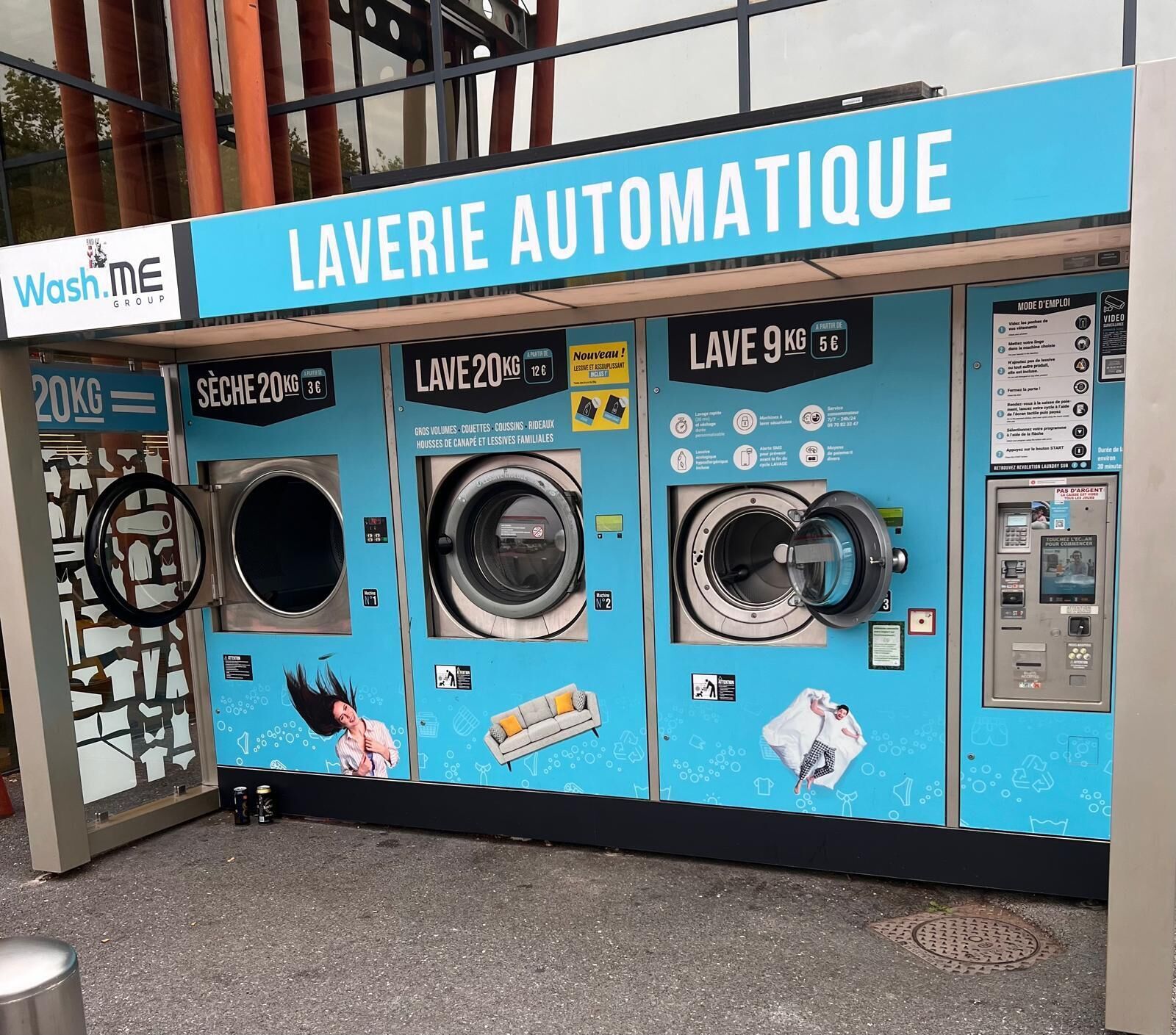 Une laverie automatique équipée de trois machines à laver, chacune étant munie d’une étiquette indiquant sa capacité et son prix.