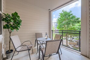 A balcony with a table and chairs, a potted plant, and a view of a tree and buildings.