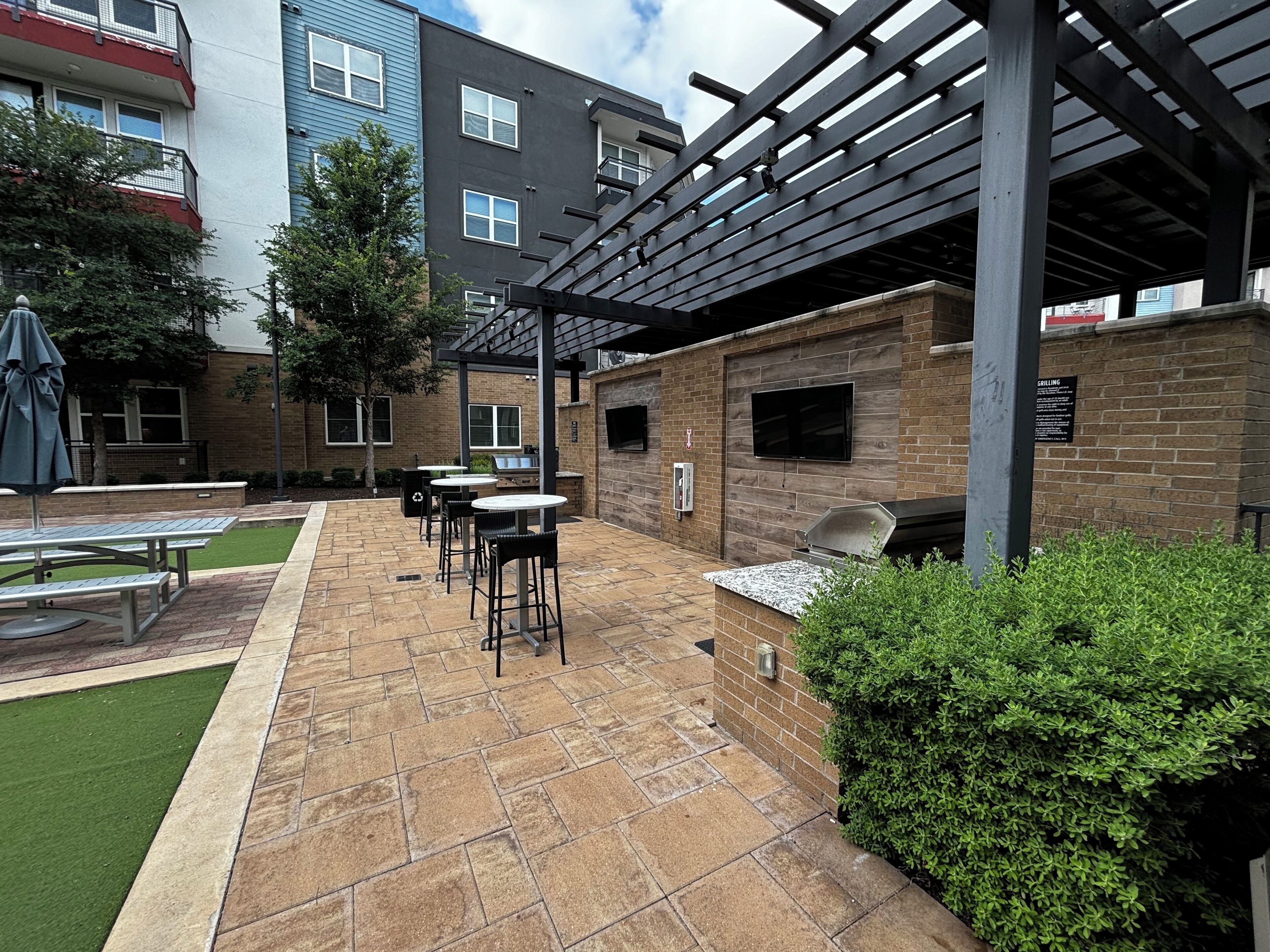 An outdoor patio area with picnic tables, a barbecue grill, and a pergola structure.
