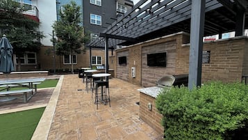 An outdoor patio area with picnic tables, a barbecue grill, and a pergola structure.