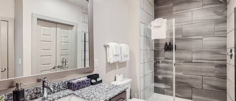 A modern bathroom with a granite countertop, a large mirror, a shower with a glass door, and a toilet.