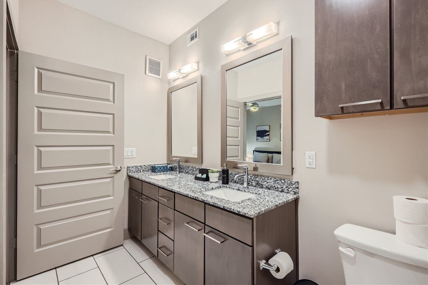 A modern bathroom with a double sink vanity, a large mirror, and a toilet.