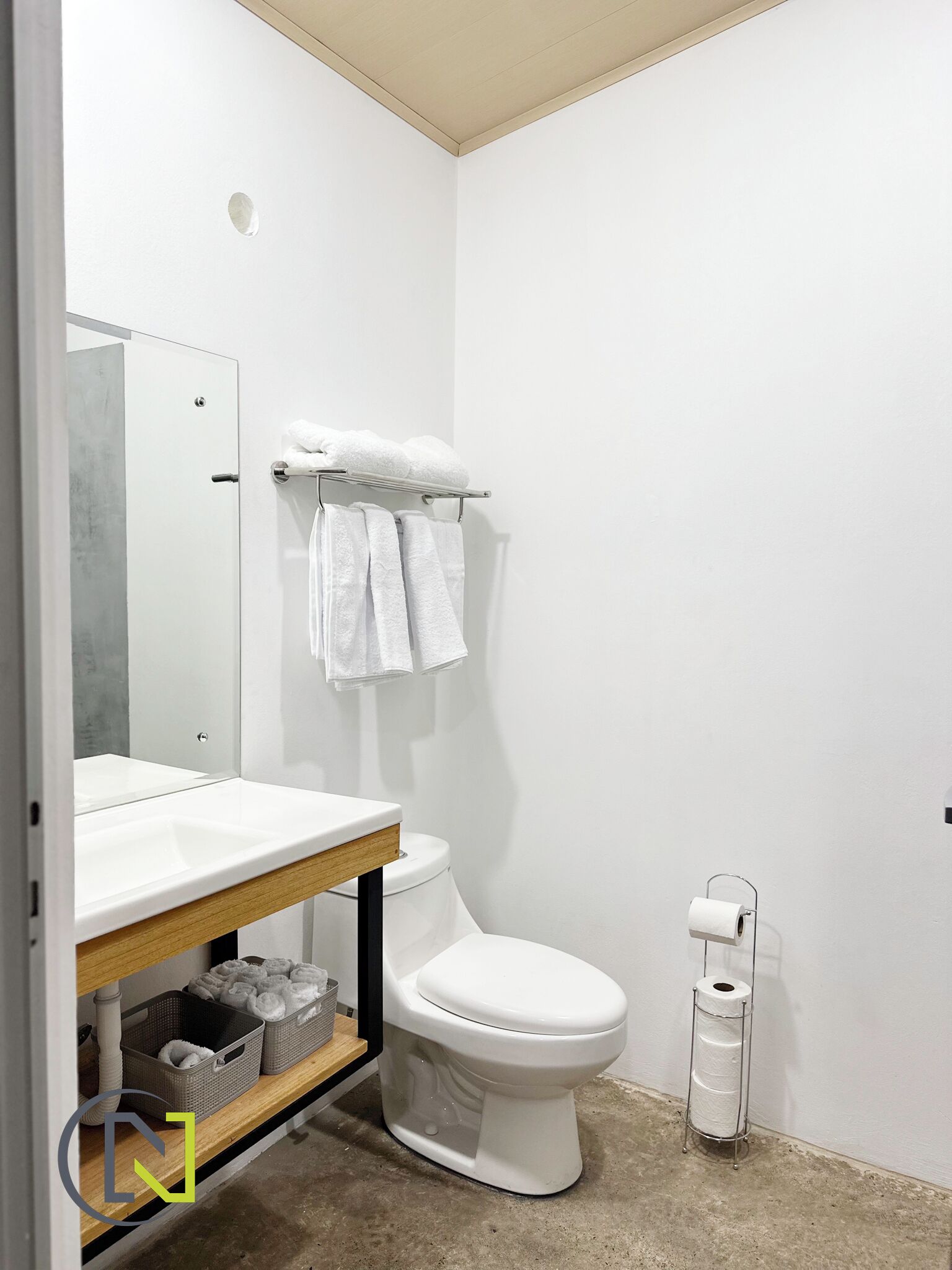 Une salle de bain moderne avec des toilettes blanches, un lavabo doté d’un plan de travail en bois et un porte-serviettes avec des serviettes blanches.