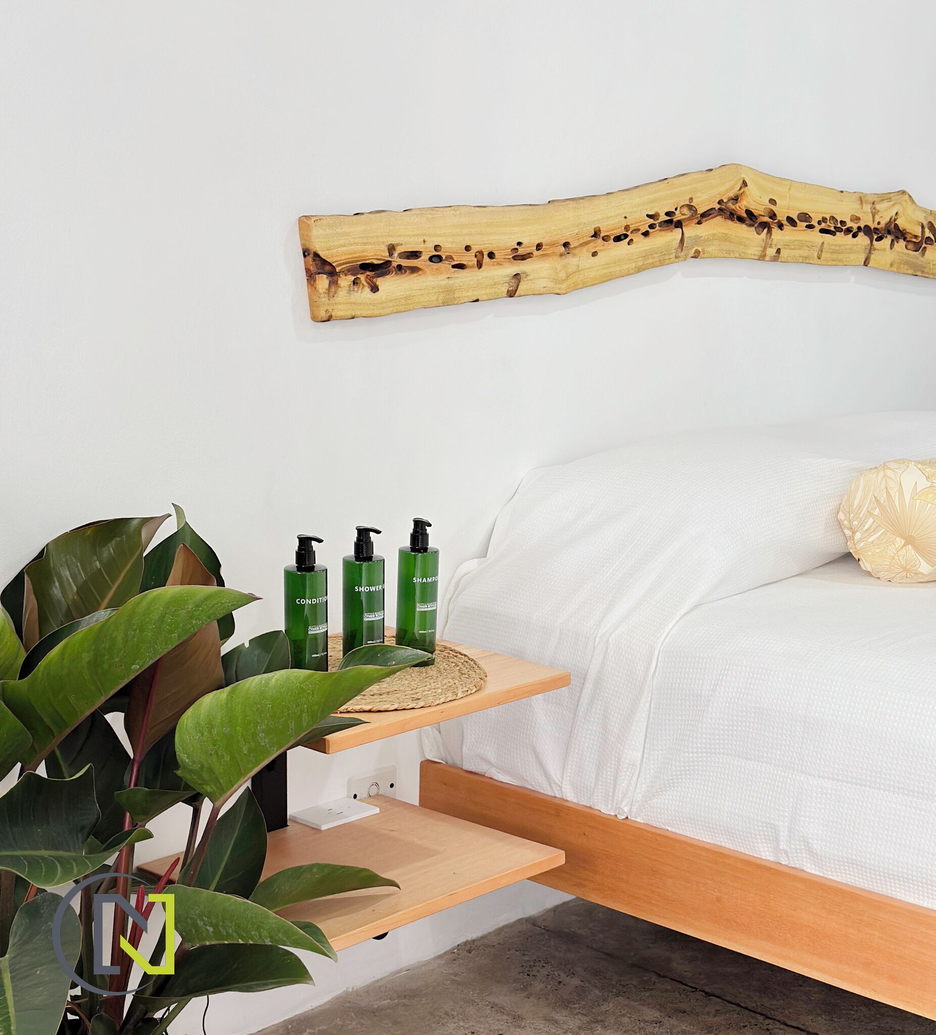 A bedroom with a wooden headboard, a bedside table with green bottles, and a large plant.