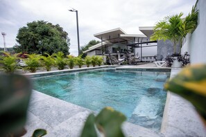 A modern outdoor pool area with a clear pool, surrounded by potted plants and a covered seating area. - Nomad Living CR (Tárcoles)