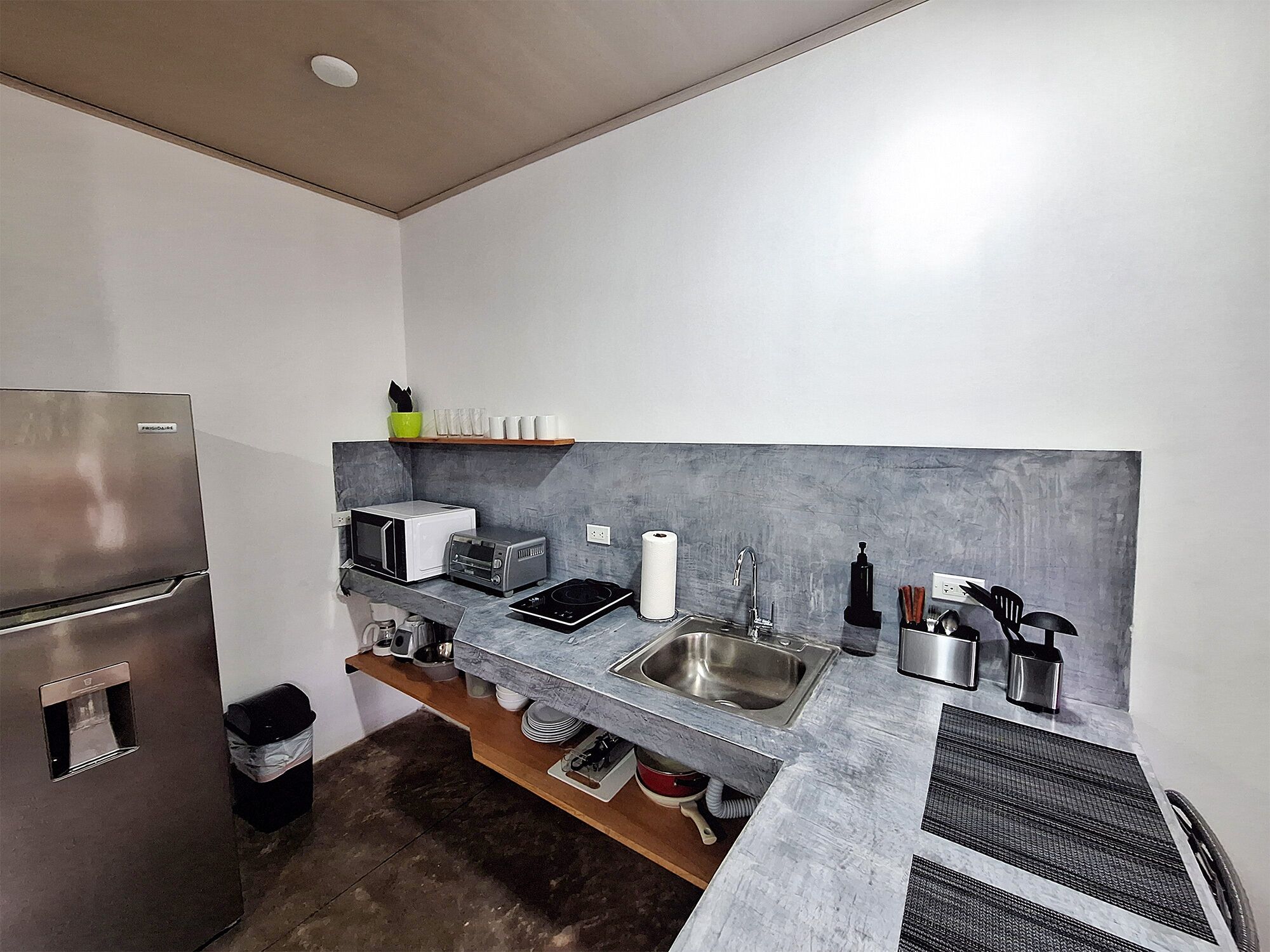 A compact kitchen with a refrigerator, microwave, toaster, sink, and various utensils.