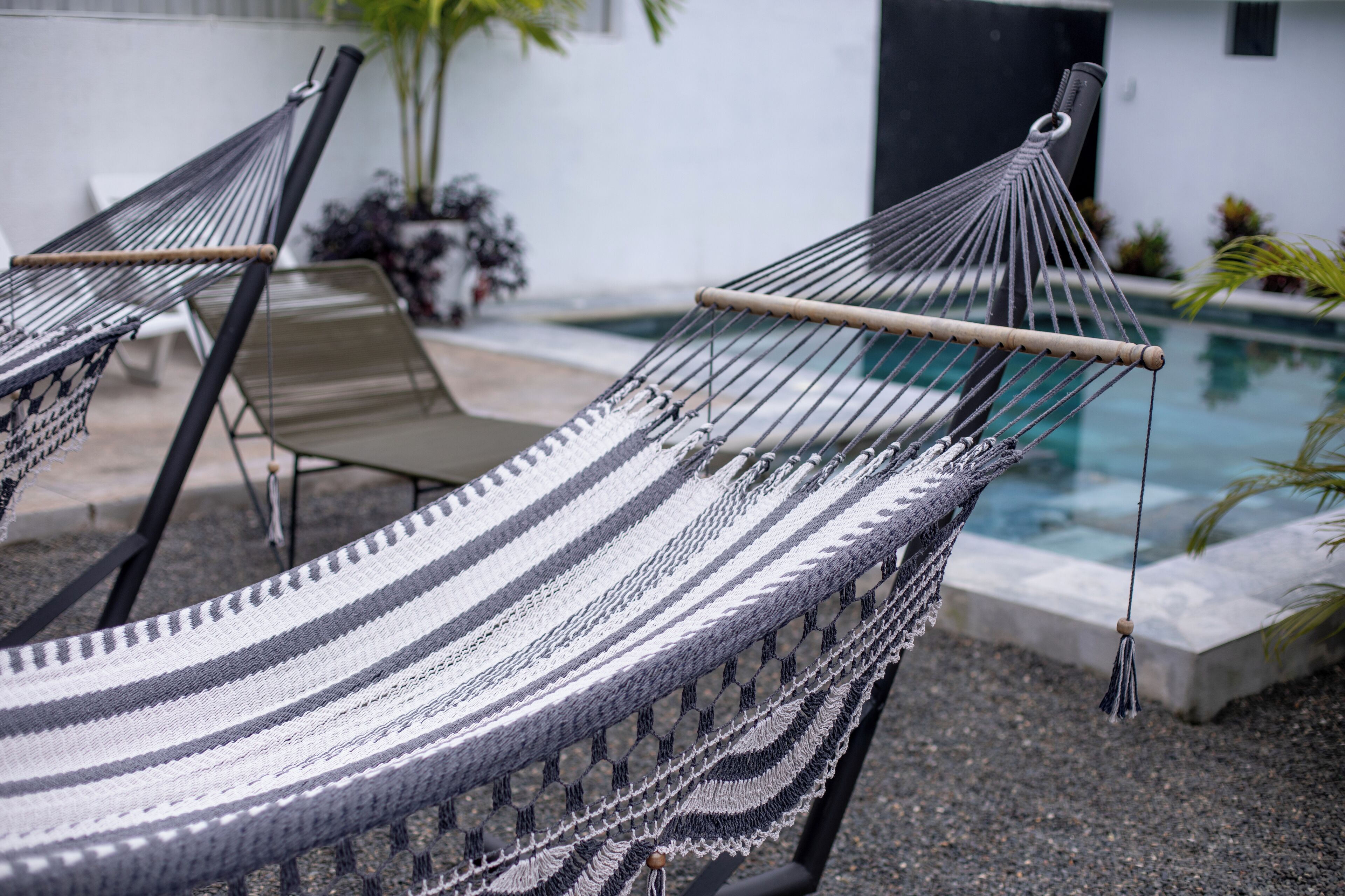 A hammock chair with a woven seat and backrest, positioned near a poolside.