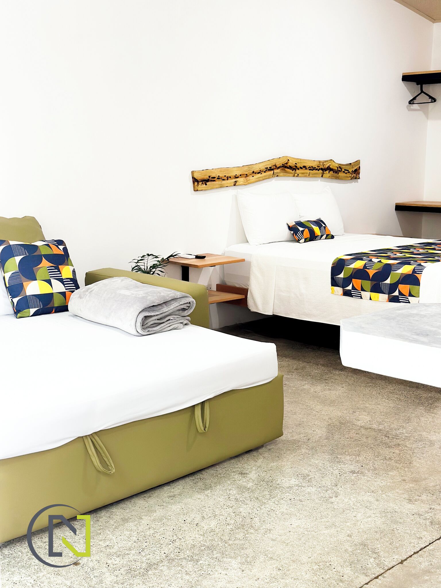 A hotel room with two beds, a wooden headboard, a small table, and a wall-mounted shelf.