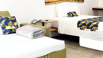 A hotel room with two beds, a wooden headboard, a small table, and a wall-mounted shelf.
