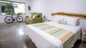 Une chambre à coucher avec un lit, un fauteuil vert, un vélo et une fenêtre ornée de plantes.