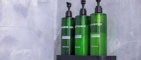 Three green bottles of shampoo, conditioner, and shower gel on a black shelf against a textured wall.