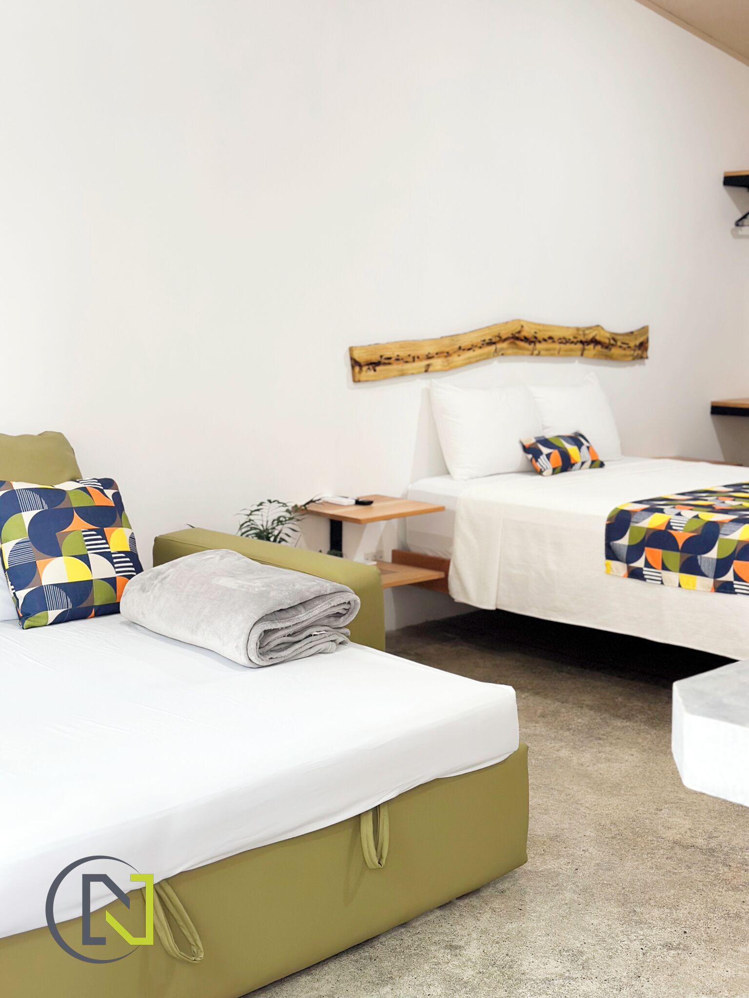 A hotel room with two beds, a wooden headboard, a small table, and a green armchair.
