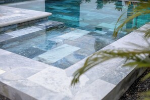 A pool with a geometric tile pattern and a stone border. - Nomad Living CR (Tárcoles)