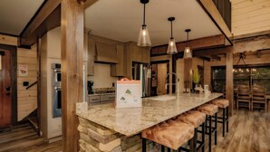 A kitchen with a stone island, bar stools, and pendant lighting. - Smoky Mountain Skies - Mountain views, gorgeous interiors, game room, hot tub, and more! (Gatlinburg)