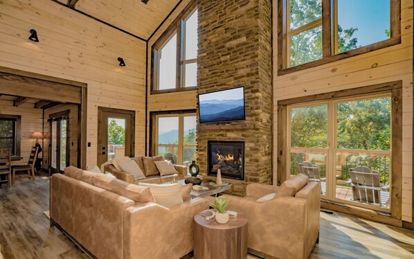 Un salón espacioso con chimenea de piedra, ventanas amplias y un televisor.