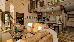 A spacious living area with a high ceiling and wooden beams, a kitchen with modern appliances, and a cozy seating area with a fireplace. - Smoky Mountain Skies - Mountain views, gorgeous interiors, game room, hot tub, and more! (Gatlinburg)