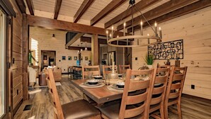 A dining area with a wooden table and chairs, a chandelier, and a wall-mounted artwork. - Smoky Mountain Skies - Mountain views, gorgeous interiors, game room, hot tub, and more! (Gatlinburg)