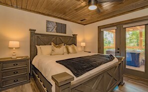 Un dormitorio con cabecera de madera, una cama grande con muchas almohadas, mesitas de noche con lámparas y vistas a una bañera de hidromasaje exterior a través de una puerta de cristal.