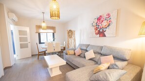 A living room with a grey sofa, white coffee table, wicker pendant light, and a floral painting on the wall. - Casa Flor del Rocío – Seville – 4 Bedrooms for 8 – AC Throughout – Terrace & Parking (La Rinconada)