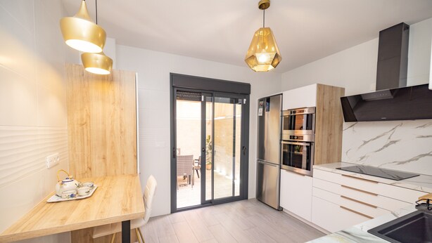 A modern kitchen with a dining area, wooden accents, and a view to the outside. - Casa Flor del Rocío – Seville – 4 Bedrooms for 8 – AC Throughout – Terrace & Parking (La Rinconada)