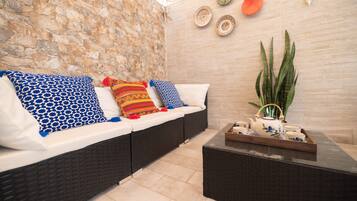 A room with a stone wall, a sofa with patterned cushions, a tray with teapot and cups, and a large plant.