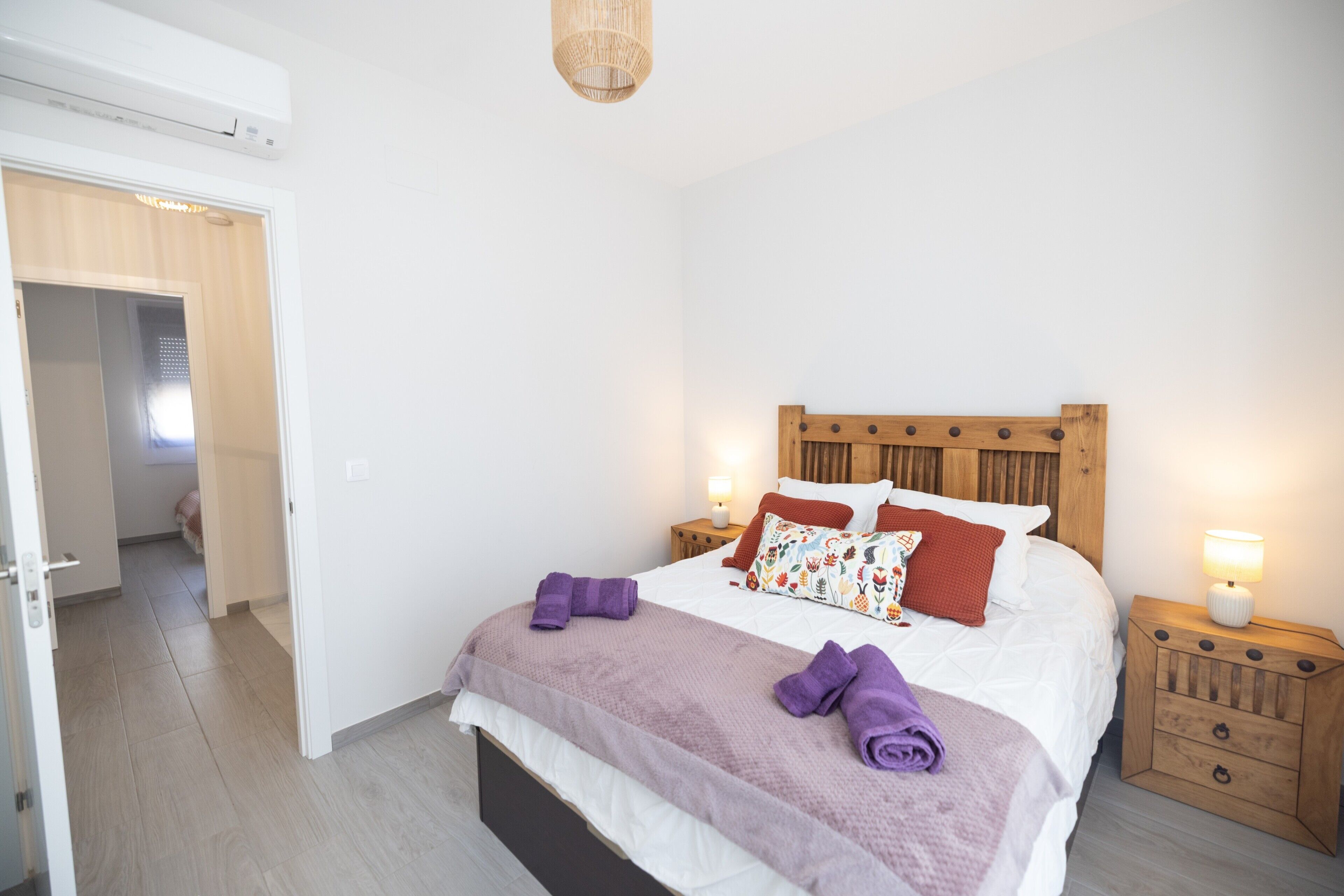 Ein Schlafzimmer mit einem Bett, Nachttischen, einem Holz-Kopfteil und einer Tür zu einem weiteren Raum.