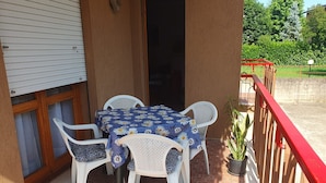 Une terrasse avec une table et des chaises, un pot de fleurs et une rambarde rouge.
