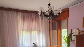Une chambre à coucher avec un lit, un lustre, des rideaux, une plante en pot et une vue à travers une porte vitrée.